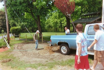 The church music director is staring at the hole, filling it with water from a hose.  Brett and Rob are walking towards him in front of a blue pickup truck.  My dad is standing behind the truck.