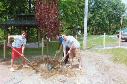 Me, Brett, and Rob holding shovels filling in a whole that contains a red tree.  They are standing on dirt, and smiling.