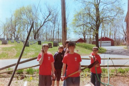 Five scouts posing for a photo.  The one of the left is holding a phone.  One in the middle is holding a shovel, ready to dig.  The one on the right is pointing a hose at the camera.